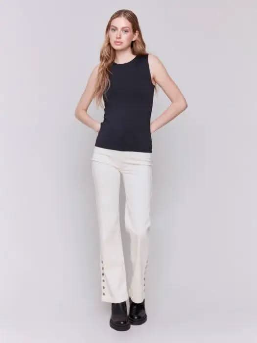 A person with long curly hair, wearing a Charlie B Super Stretch Sleeveless Top, blue jeans, and black ankle boots, stands posing against a plain background.