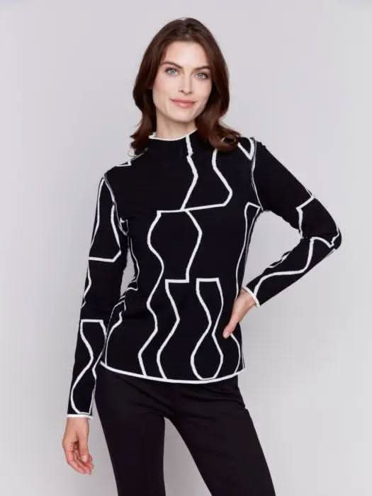 A person wearing the Reversible Jacquard Mock Neck Sweater by Charlie B, featuring black abstract patterns, stands with their back to the camera, showcasing an essential piece for any winter wardrobe.