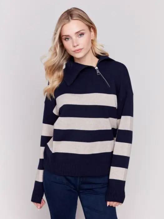 A person with light-colored hair wears a high-quality Charlie B Striped Turtleneck with Side Zip in navy and white, paired with dark pants against a plain background.