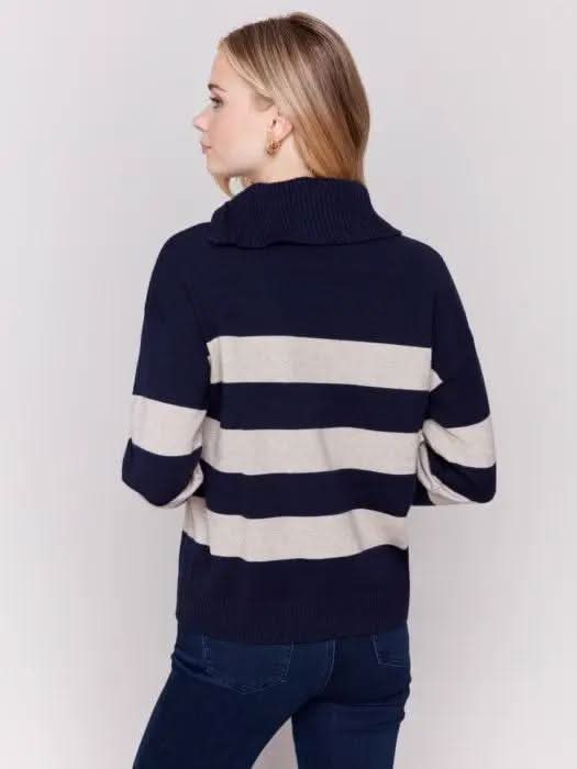 A person with light-colored hair wears a high-quality Charlie B Striped Turtleneck with Side Zip in navy and white, paired with dark pants against a plain background.
