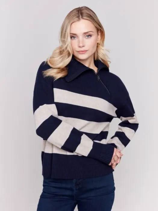 A person with light-colored hair wears a high-quality Charlie B Striped Turtleneck with Side Zip in navy and white, paired with dark pants against a plain background.