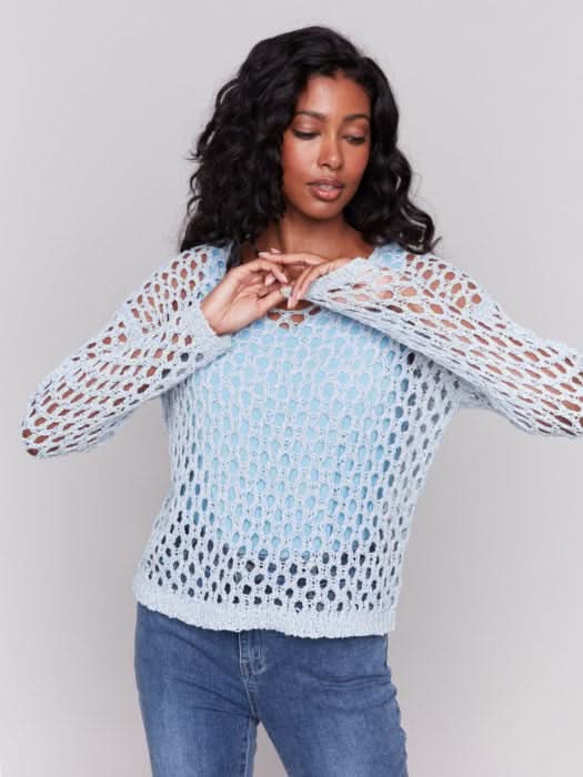 A person wearing the Charlie B Braided Fishnet V-Neck Sweater in light blue with jeans stands against a plain gray background.