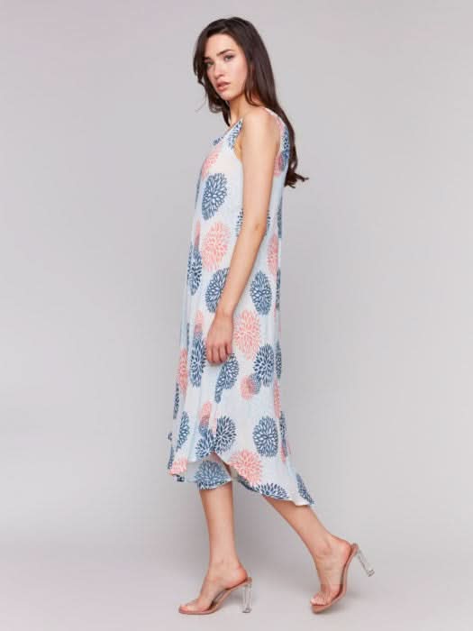 Against a plain backdrop, someone showcases Charlie B’s Sleeveless Printed Rayon Dress, featuring breathable rayon fabric and a charming blue and pink floral pattern with an asymmetrical hemline.