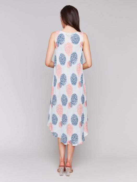 Against a plain backdrop, someone showcases Charlie B’s Sleeveless Printed Rayon Dress, featuring breathable rayon fabric and a charming blue and pink floral pattern with an asymmetrical hemline.