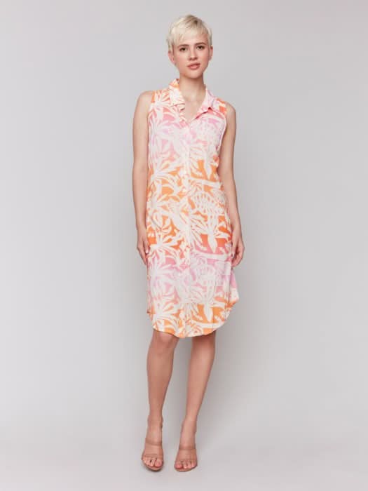 A person with short blonde hair wears the Charlie B Printed Sleeveless Button-Front Dress with a pink and orange leaf pattern and beige heels, standing against a plain light background.