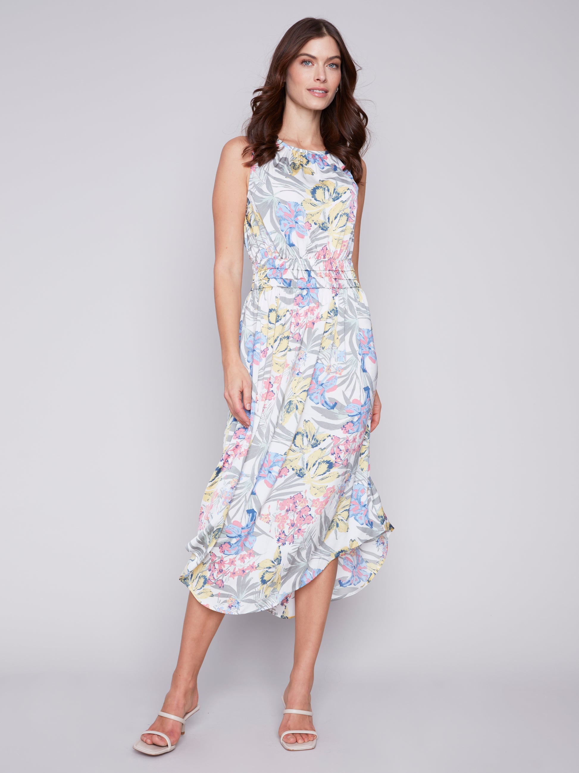 A woman in a Charlie B Petal Path Sleeveless Dress with Elastic Smocking Waist posing against a neutral background.