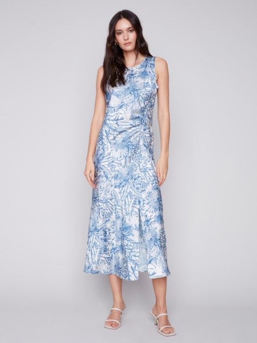 A woman in a blue and white jungle print Charlie B sleeveless long satin dress, standing against a light gray background. She is wearing light sandals.