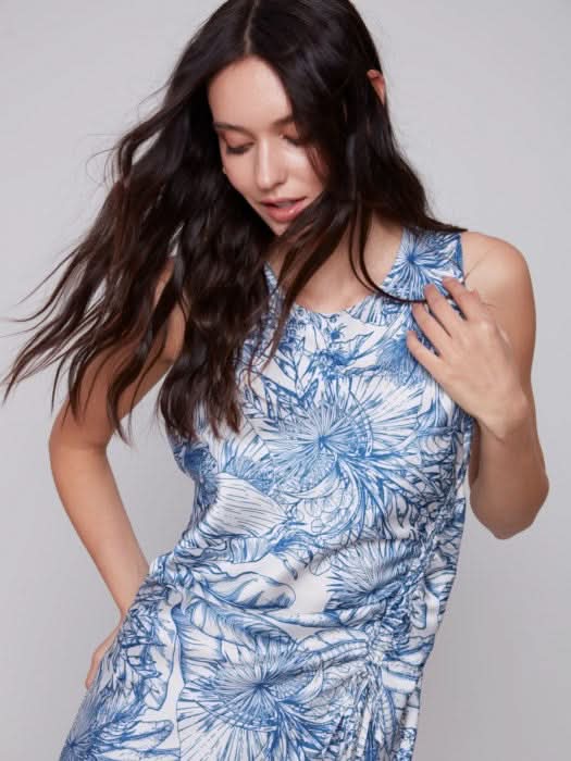 A woman in a blue and white jungle print Charlie B sleeveless long satin dress, standing against a light gray background. She is wearing light sandals.