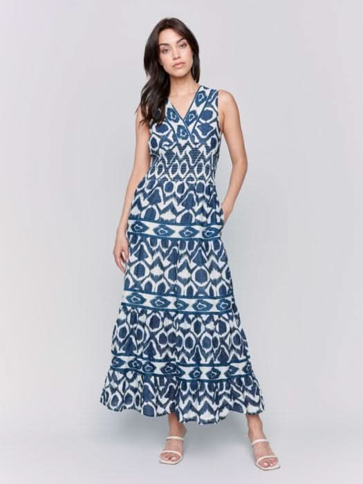 A person is wearing a Charlie B Sleeveless Cotton Maxi Dress with blue and white patterns and ruffled tiers, ideal as a breathable summer dress, against a plain gray background.