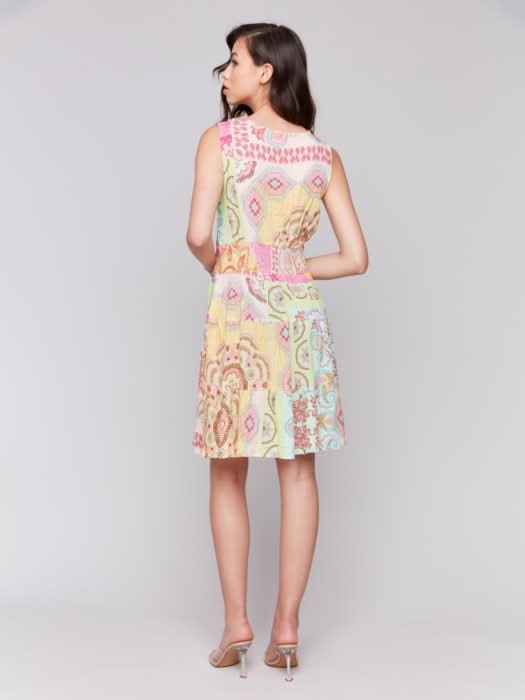 A woman models the Charlie B Sleeveless V-Neck Tiered Dress with a colorful patchwork pattern and neutral heels, embodying chic summer style against a plain background.