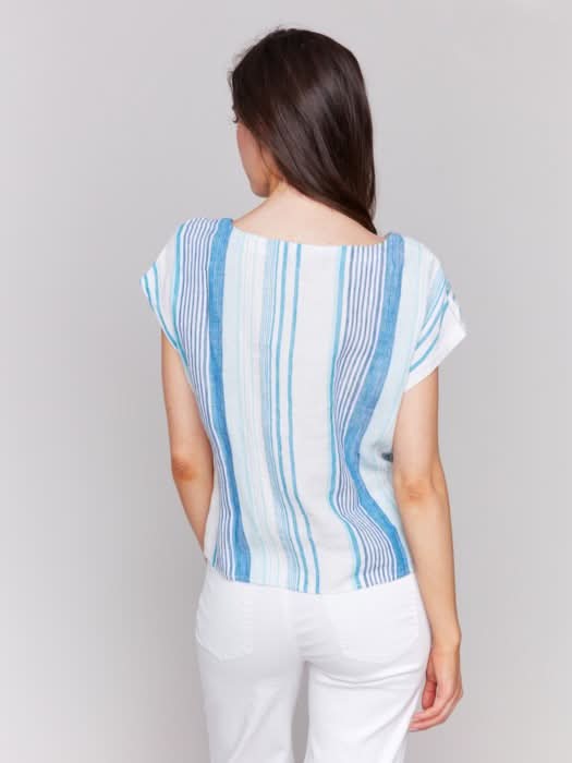A woman models the Charlie B Striped Linen Blend Top with Front Tie and white pants against a light background—an effortless summer wardrobe choice.
