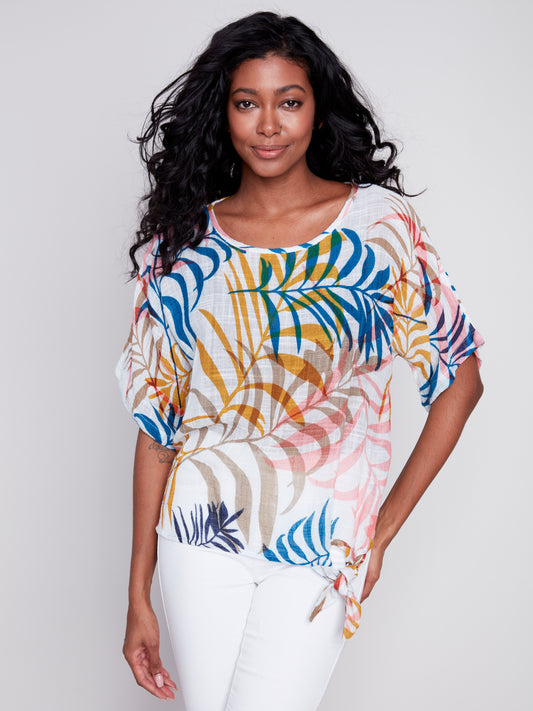 A woman wearing a high-quality cotton Charlie B Dolman Cotton Printed Blouse With Side Tie with a colorful tropical digital print.