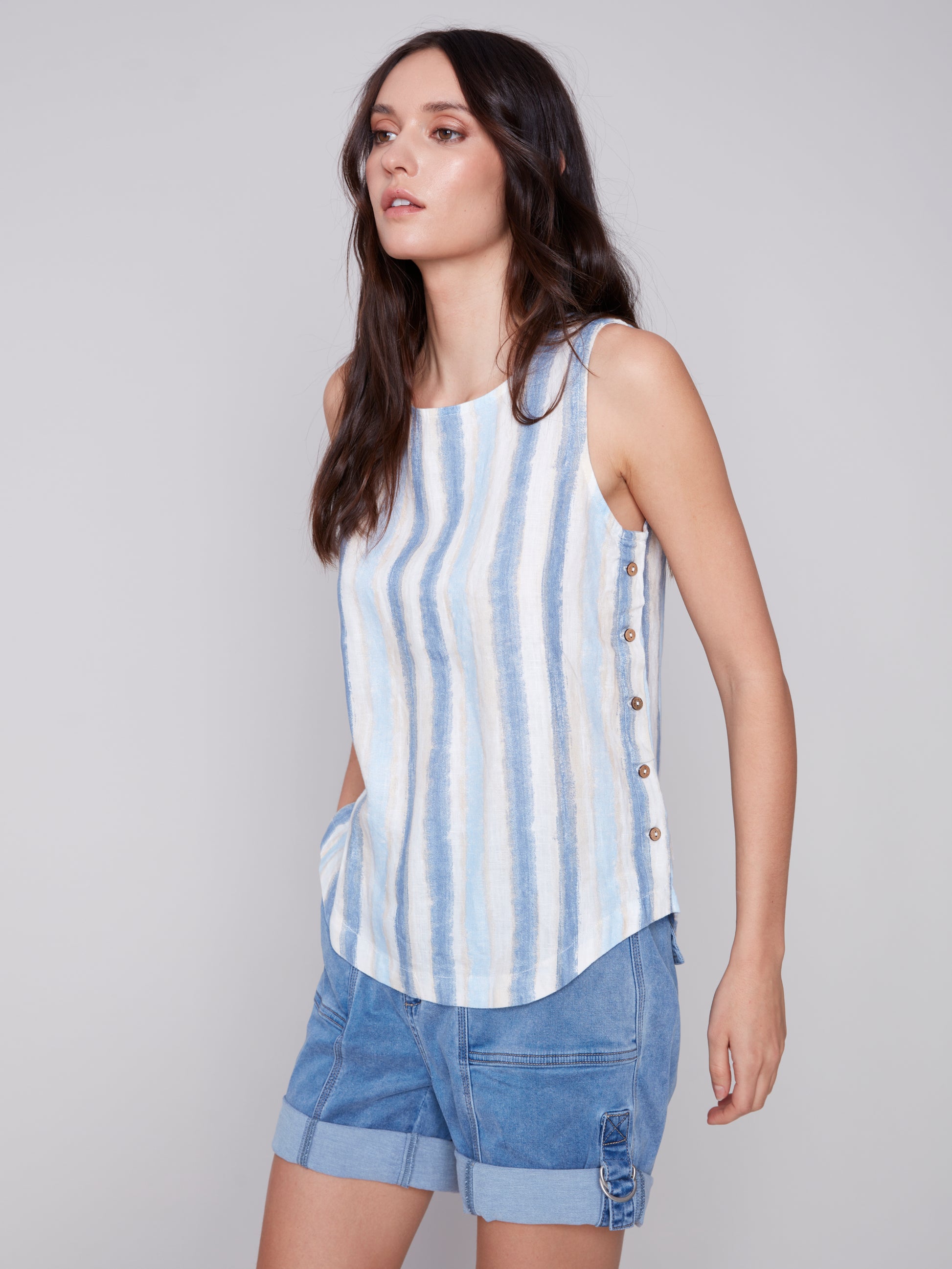 The model is wearing a stylish Charlie B Linen Top with Side Buttons in blue stripes.