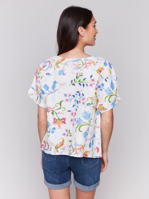 A woman stands against a plain background wearing the Charlie B Printed Linen Short Dolman Sleeve Top, light green cropped pants, and nude heeled sandals.