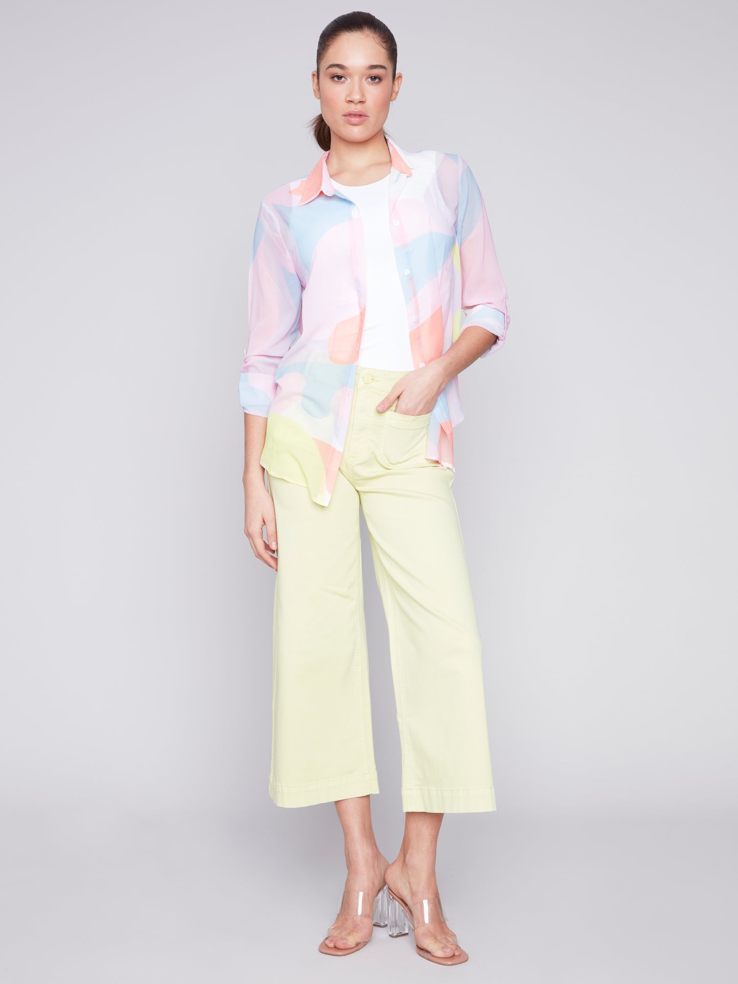 Woman posing in a Charlie B printed chiffon blouse with a cute design and light yellow pants.