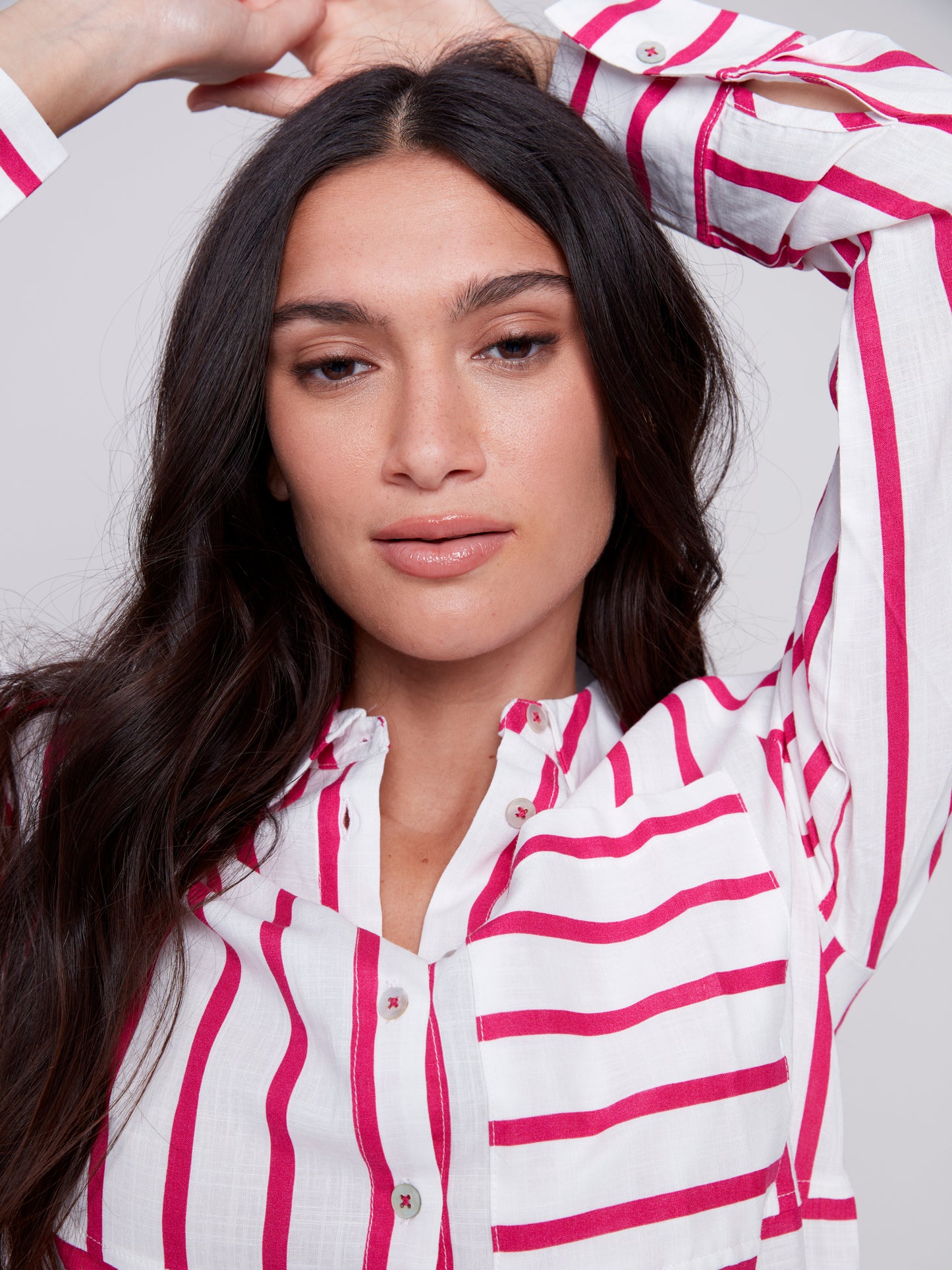 Woman wearing a Charlie B Lined Blend Striped 3/4 Button Top with white pants posing against a gray background.