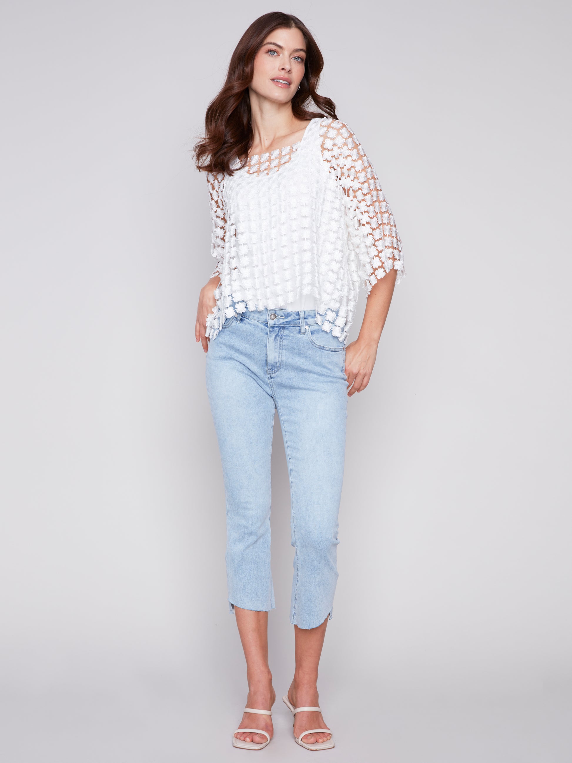 A woman wearing jeans and a white Charlie B Flower Embroidered Blouse.