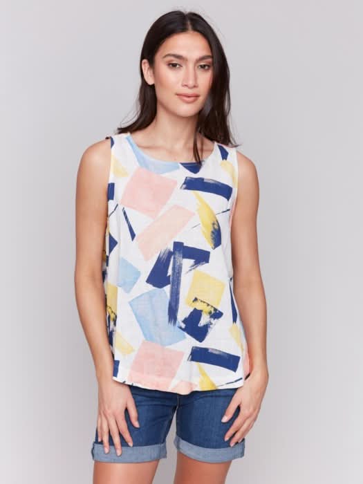 A woman stands against a plain background wearing the Charlie B Printed Sleeveless Top with Rounded Hem and denim shorts—a true summer favorite.
