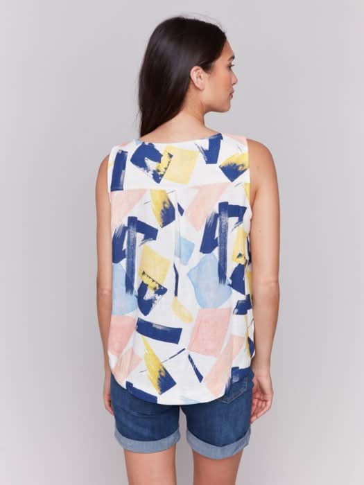A woman stands against a plain background wearing the Charlie B Printed Sleeveless Top with Rounded Hem and denim shorts—a true summer favorite.