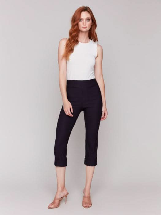 Rear view of someone wearing flattering pink Stretch Pull-On Capri Pants by Charlie B and a white top, standing in heels against a neutral background.