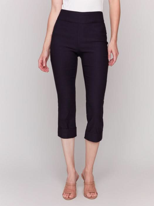 Rear view of someone wearing flattering pink Stretch Pull-On Capri Pants by Charlie B and a white top, standing in heels against a neutral background.