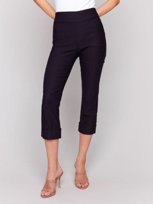 Rear view of someone wearing flattering pink Stretch Pull-On Capri Pants by Charlie B and a white top, standing in heels against a neutral background.