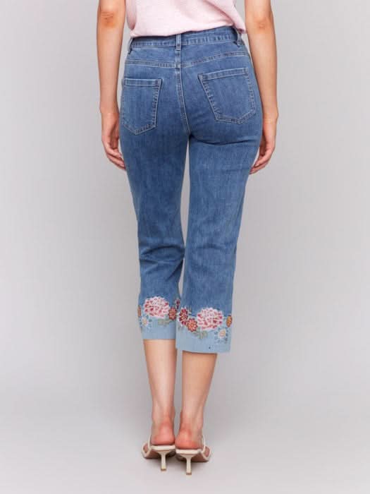 A woman in a pink T-shirt and Charlie B's Embroidered Cuff Cropped Jeans poses against a gray background.