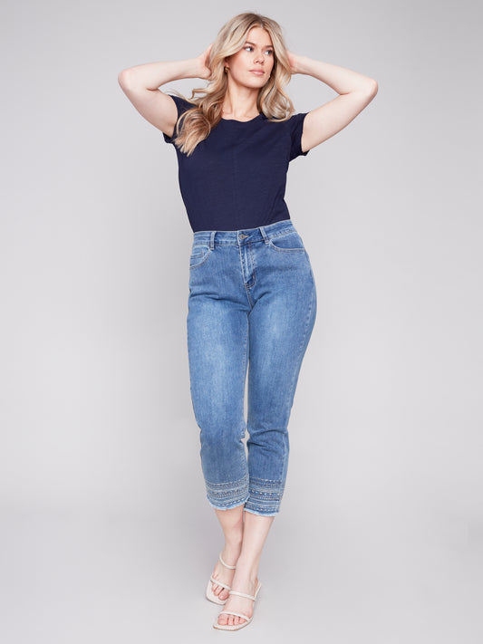A woman in a medium blue top and jeans is posing for a photo wearing Charlie B's Embroidered Hem Pant.