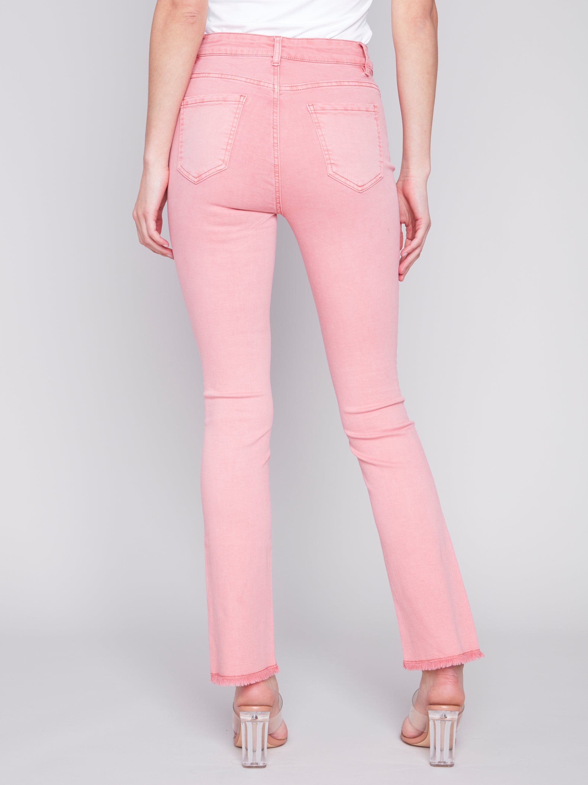 A woman wearing timeless design pink jeans with Charlie B's Asymmetrical Frayed Hem Bell Bottoms and a white top.