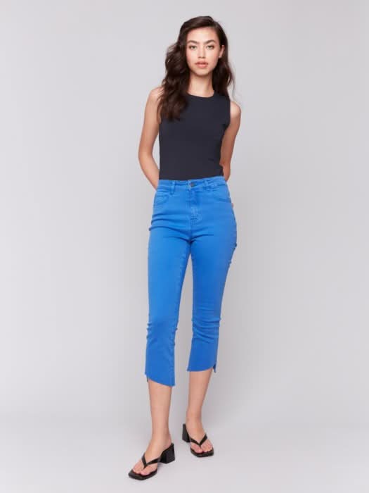 Model wears Charlie B Stretch Cropped Pants with Asymmetrical Hem in bright blue and black heeled sandals, photographed from the back against a light background, showcasing modern style and versatile wear.