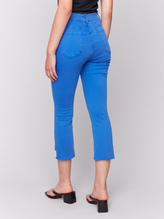 Model wears Charlie B Stretch Cropped Pants with Asymmetrical Hem in bright blue and black heeled sandals, photographed from the back against a light background, showcasing modern style and versatile wear.