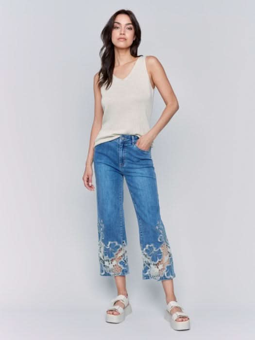 A woman is wearing Charlie B's Crop Flare Leg Jeans with a laser cut lace hem, paired with white platform sandals.