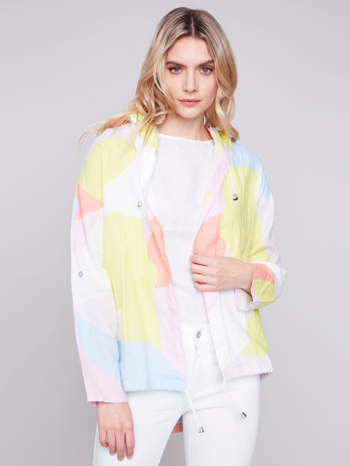 Woman wearing a Charlie B Graffiti Duster Jacket and white pants against a grey background.