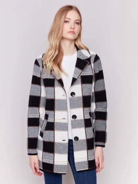 A woman with long hair, standing against a plain background and showcasing her winter wardrobe, is wearing the Charlie B Knit Plaid Coat along with jeans.
