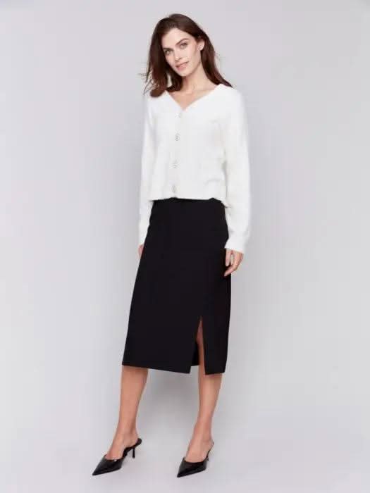 A person wearing a white long-sleeve shirt, a Charlie B Gutsy Crepe Skirt with Patch Pockets, and black pointed mules stands against a plain background.