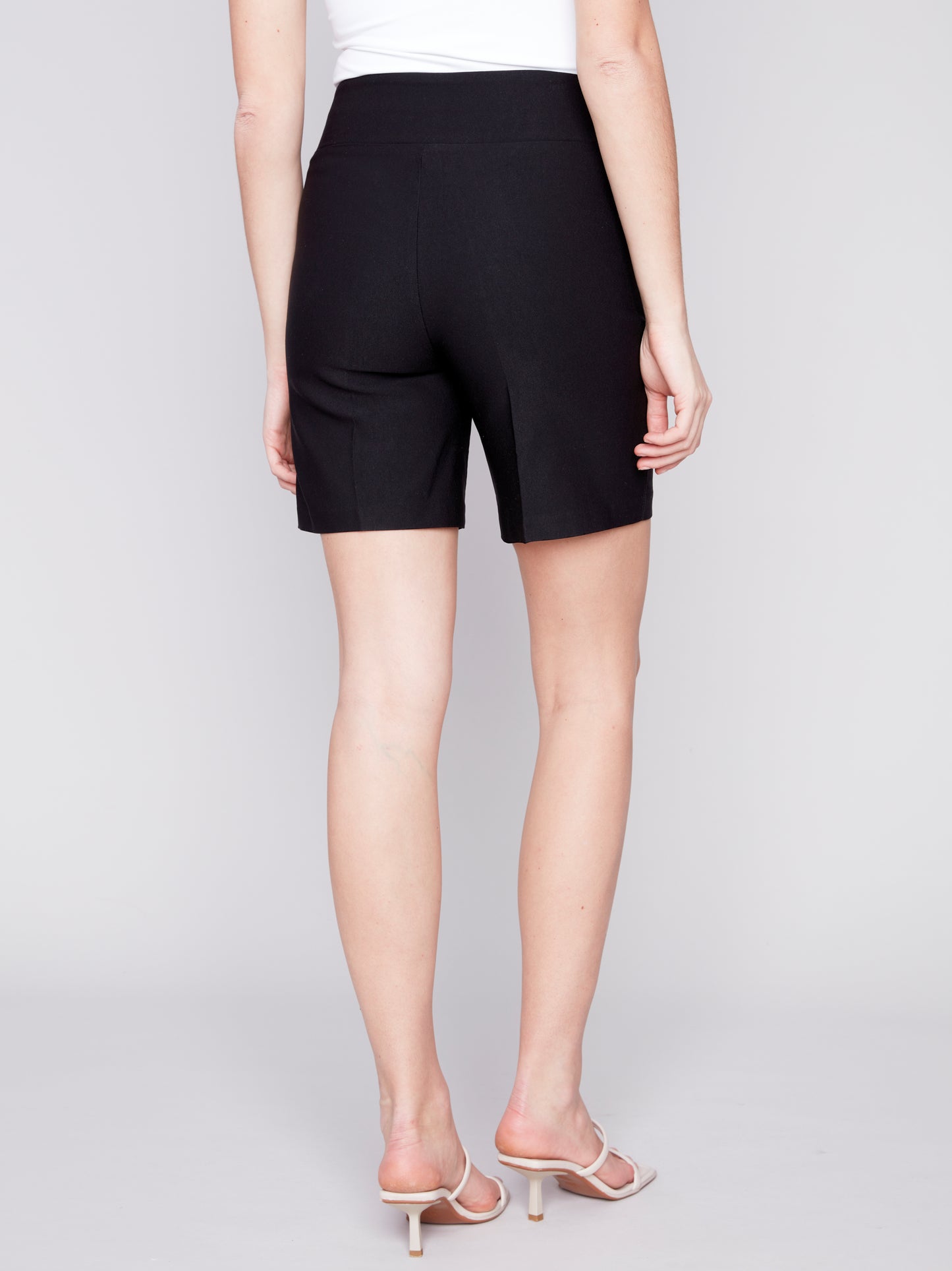 A woman wearing Charlie B smooth stretch shorts in black, paired with a stylish white top, showcasing both comfort and style.