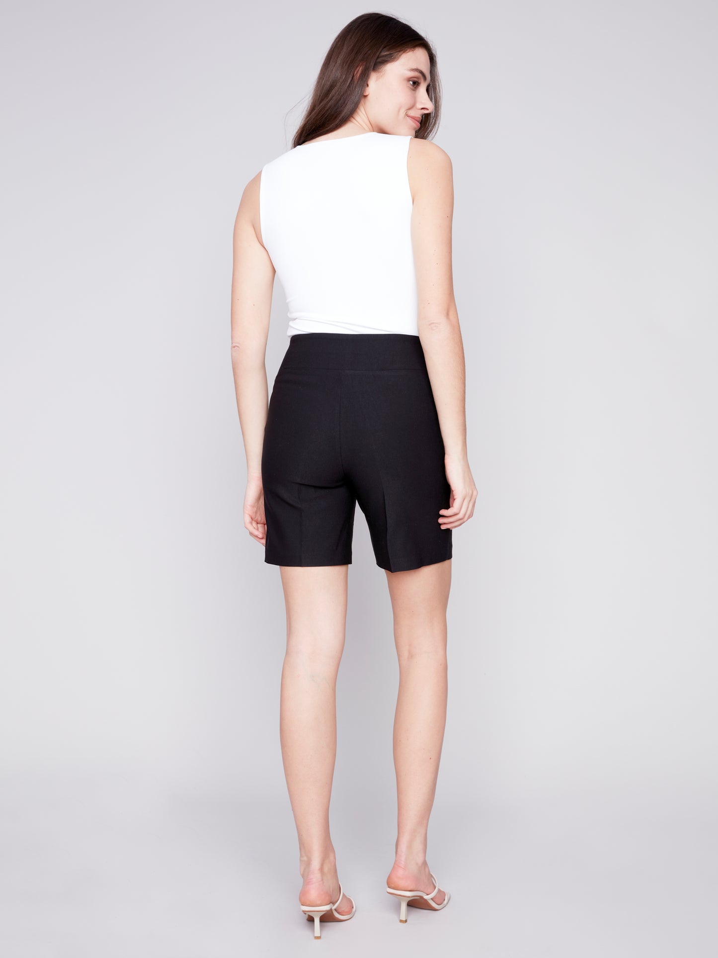 A woman wearing Charlie B smooth stretch shorts in black, paired with a stylish white top, showcasing both comfort and style.