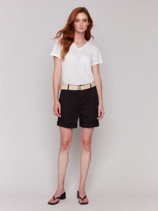A fashionista against a plain background wears chic Charlie B Cuffed Shorts with a light belt, a crisp white top, and stylish black sandals.