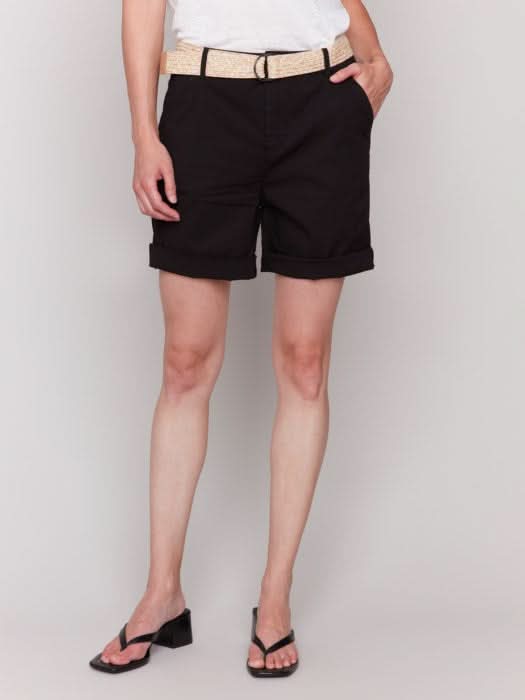 A fashionista against a plain background wears chic Charlie B Cuffed Shorts with a light belt, a crisp white top, and stylish black sandals.