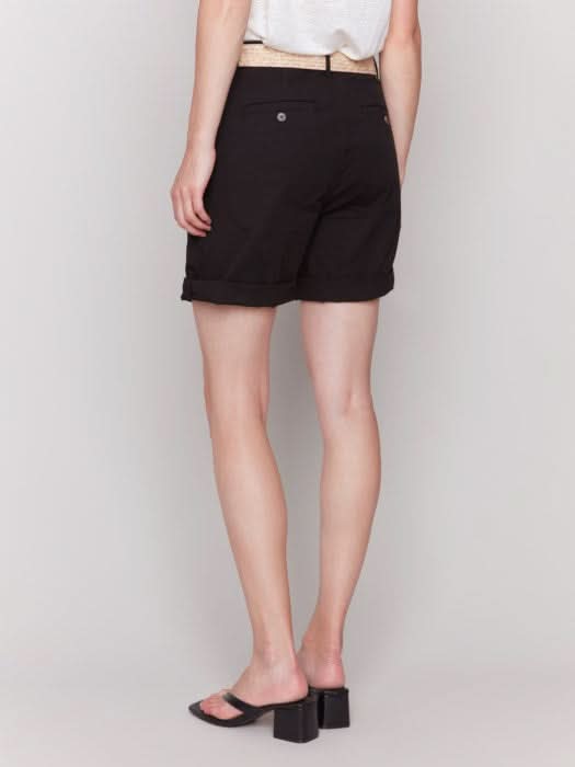 A fashionista against a plain background wears chic Charlie B Cuffed Shorts with a light belt, a crisp white top, and stylish black sandals.