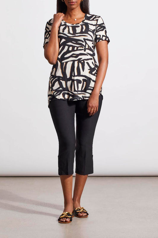 A woman stands wearing a Tribal crew neck top with buttons crafted from the finest materials, cropped black pants, and patterned sandals.