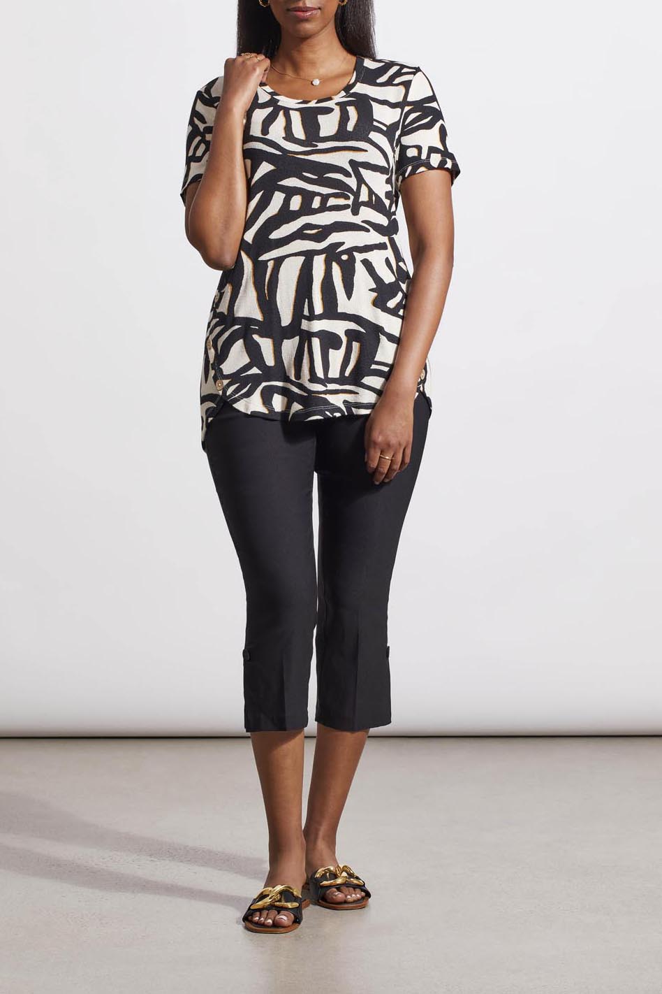 A woman stands wearing a Tribal crew neck top with buttons crafted from the finest materials, cropped black pants, and patterned sandals.