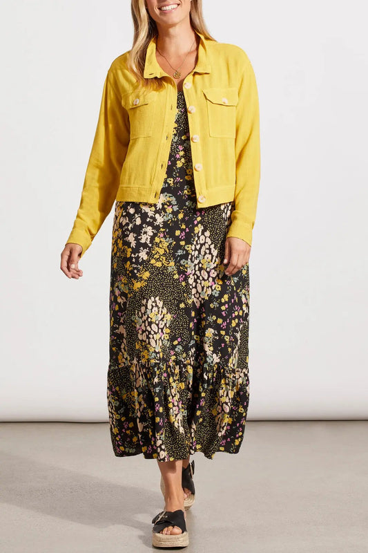 A person wearing a stylish yellow Tribal cropped jacket with pockets with a floral dress and black sandals.