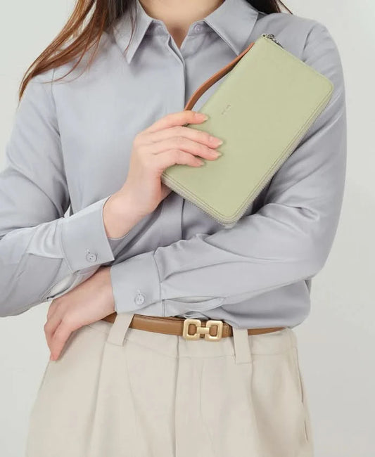 A woman in a light gray button-up shirt and beige pants holds Co-Lab’s sustainable 'ALEXX' Wallet in light green near her chest.