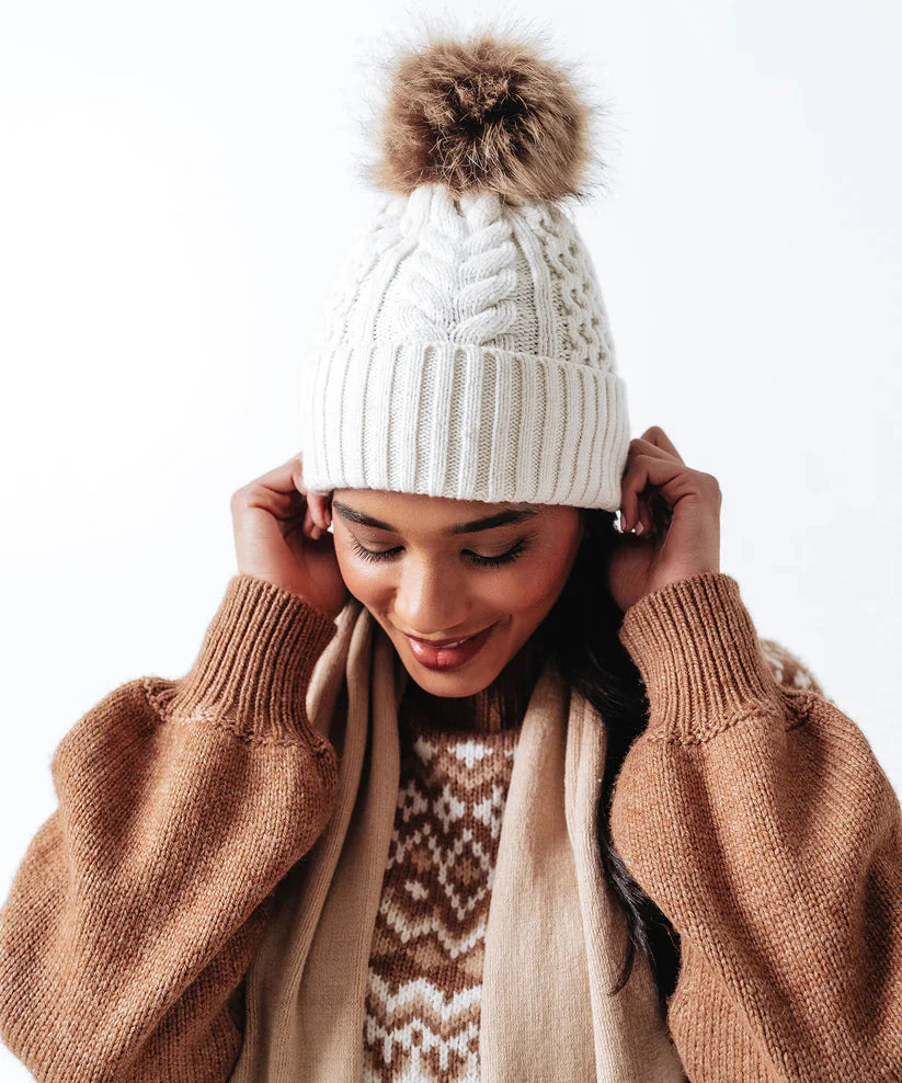 A woman wearing an Echo New York Recycled Wishbone Cable Pom Hat.
