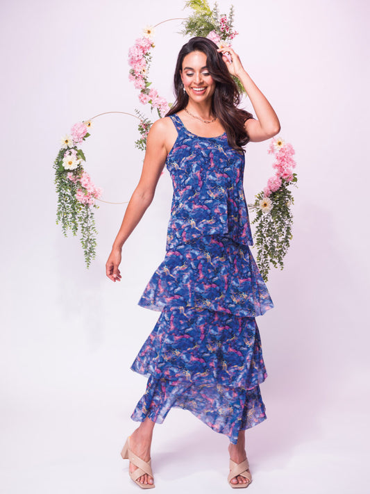 Woman in an Elana Wang Tiered Round Neck Dress in Blue posing with a hand on her head, standing in front of a decorative floral hoop.