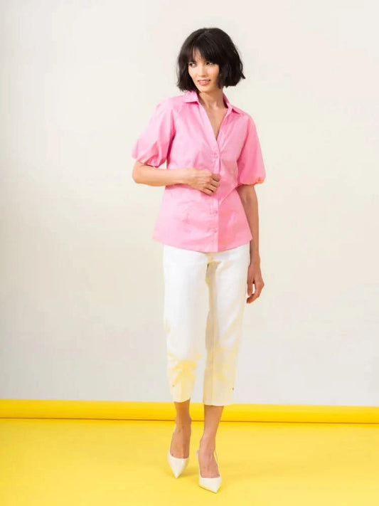 A person poses against a pale background, highlighting the Pink Puffy Blouse by Elena Wang, complemented by white pants and heels, all made from high-quality materials.