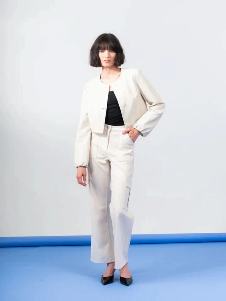 A person with short dark hair models a chic ensemble featuring Elena Wang's Detachable Zip Up Jacket in cream, paired with matching wide-legged trousers. The black top and pointed shoes provide contrasting elegance to complete this stylish look against a simple backdrop.