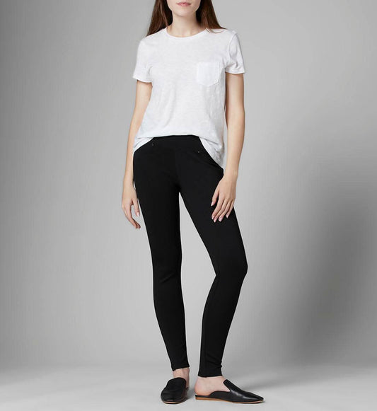 A person stands against a plain background wearing a white t-shirt, black Ricki Skinny Leggings by Jag with a mid-rise waistline, and black slip-on shoes.