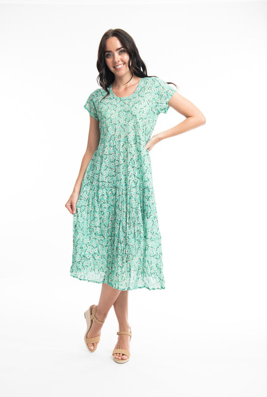 A woman in a Orientique Sweet Bias Green Dress smiling and posing with one hand on her hip against a white background.